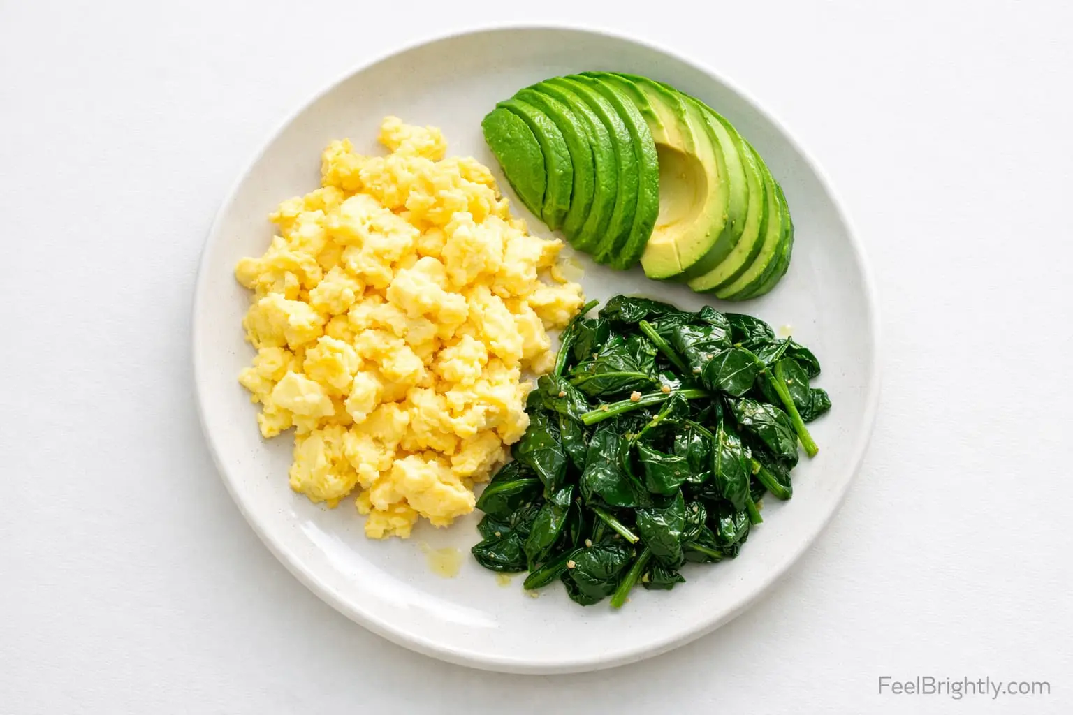 Simple keto breakfast plate with scrambled eggs, avocado slices, and sauteed spinach on white plate - clean fuel that lasts for hours - FeelBrightly.com